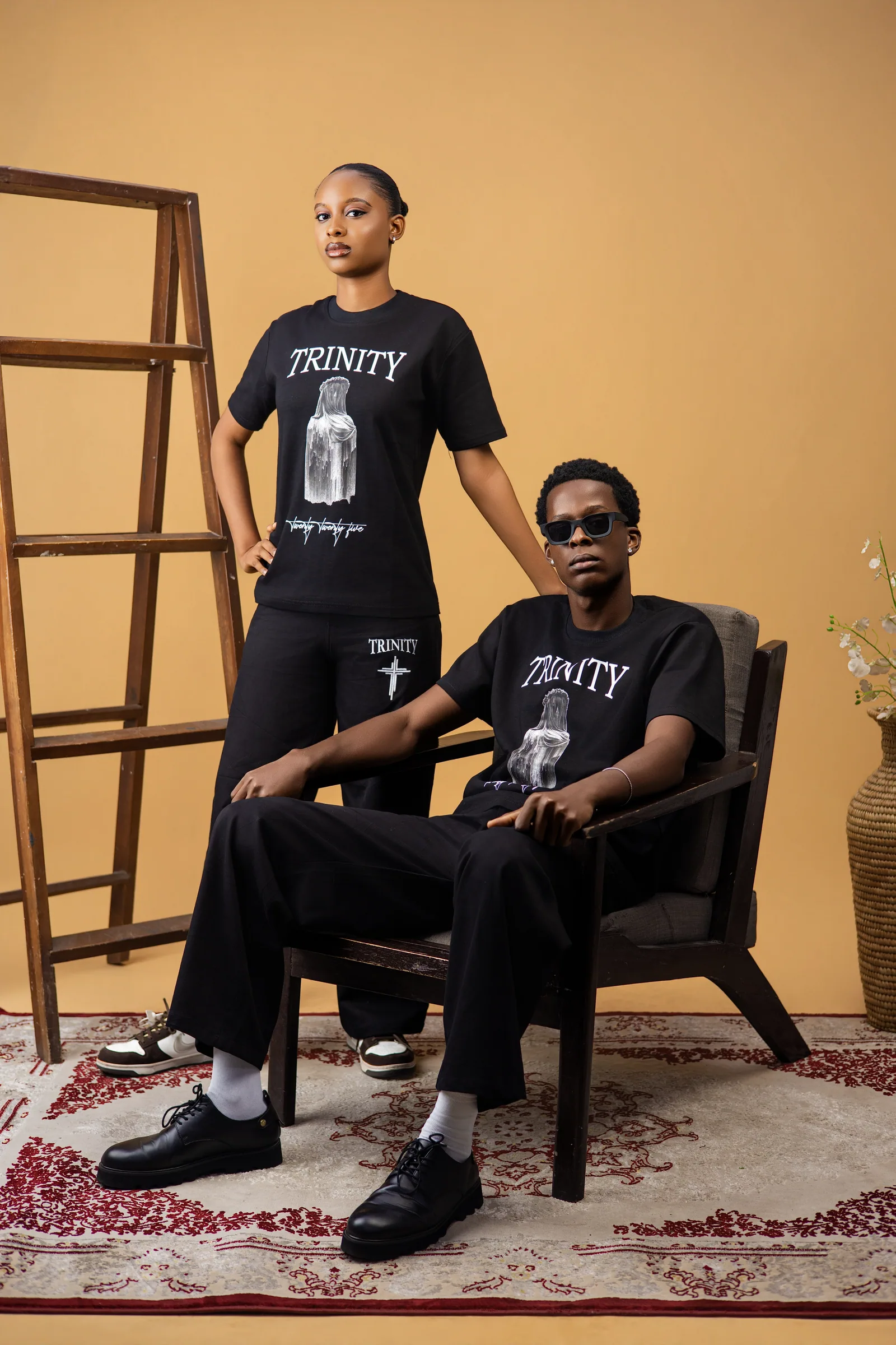 Male model seated and female model standing, both in the black shirt and pants
